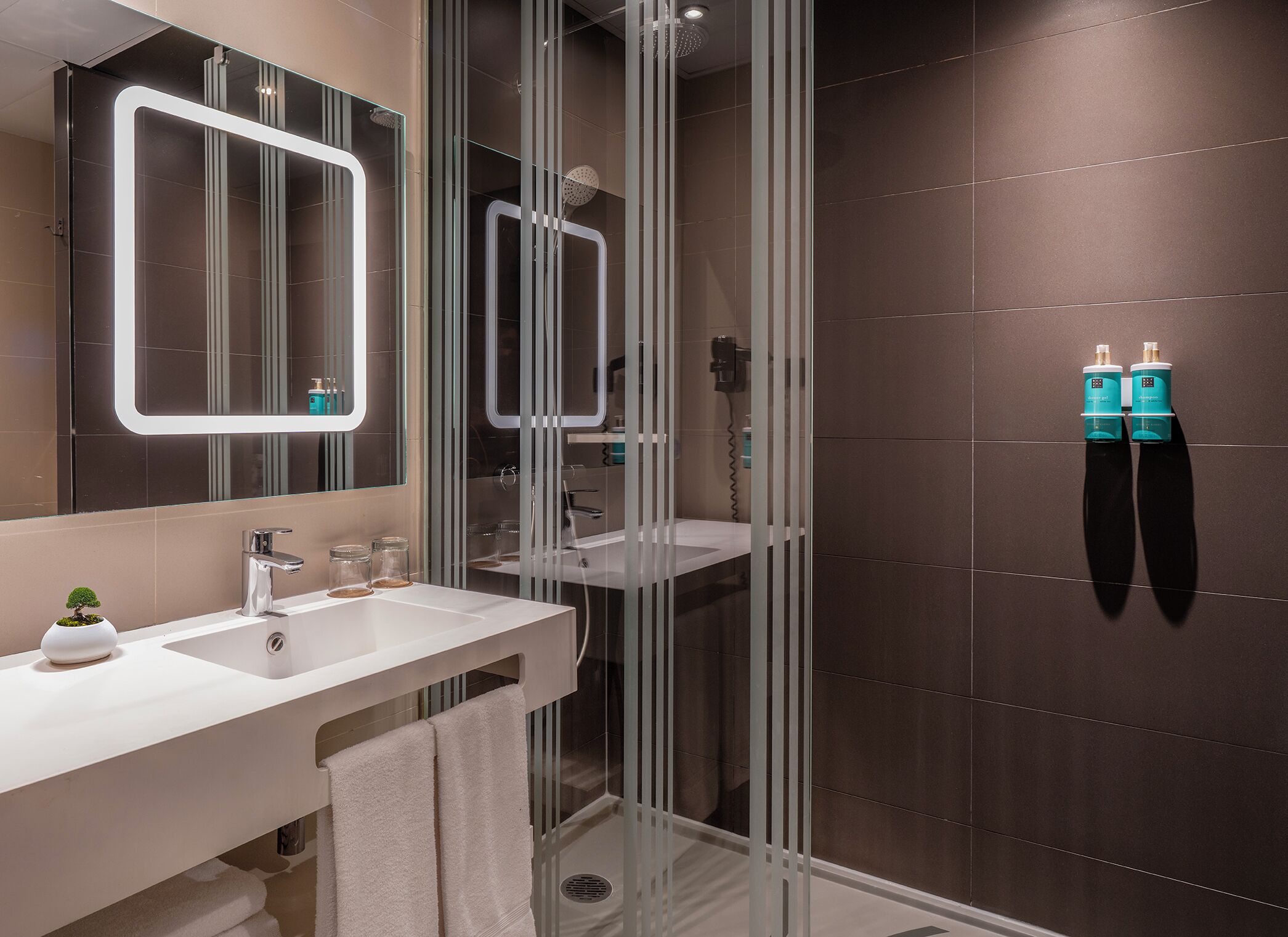 A modern bathroom with a glass shower enclosure, a large mirror, and two bottles of shampoo on the wall.