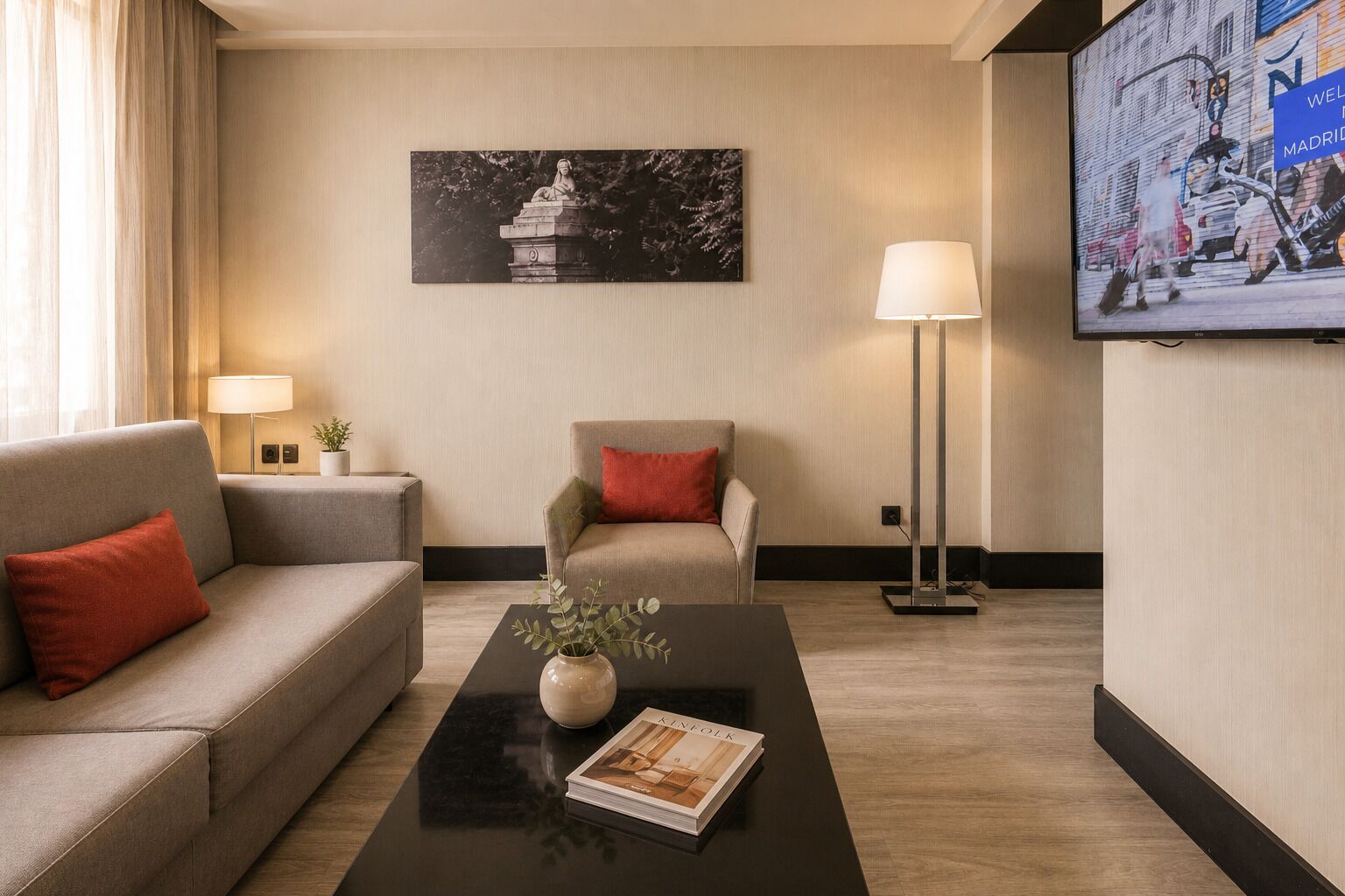 Une chambre d’hôtel équipée d’un canapé, d’un fauteuil, d’une table basse, d’une lampe, d’une télévision et d’un tableau au mur.