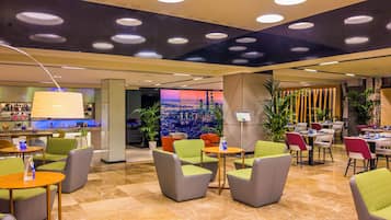 Un moderno vestíbulo de hotel con zonas de estar, un bar y un amplio ventanal con vistas a la ciudad.