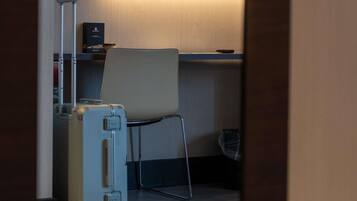 Una habitación pequeña con una sola silla, una maleta y un televisor sobre un mueble.