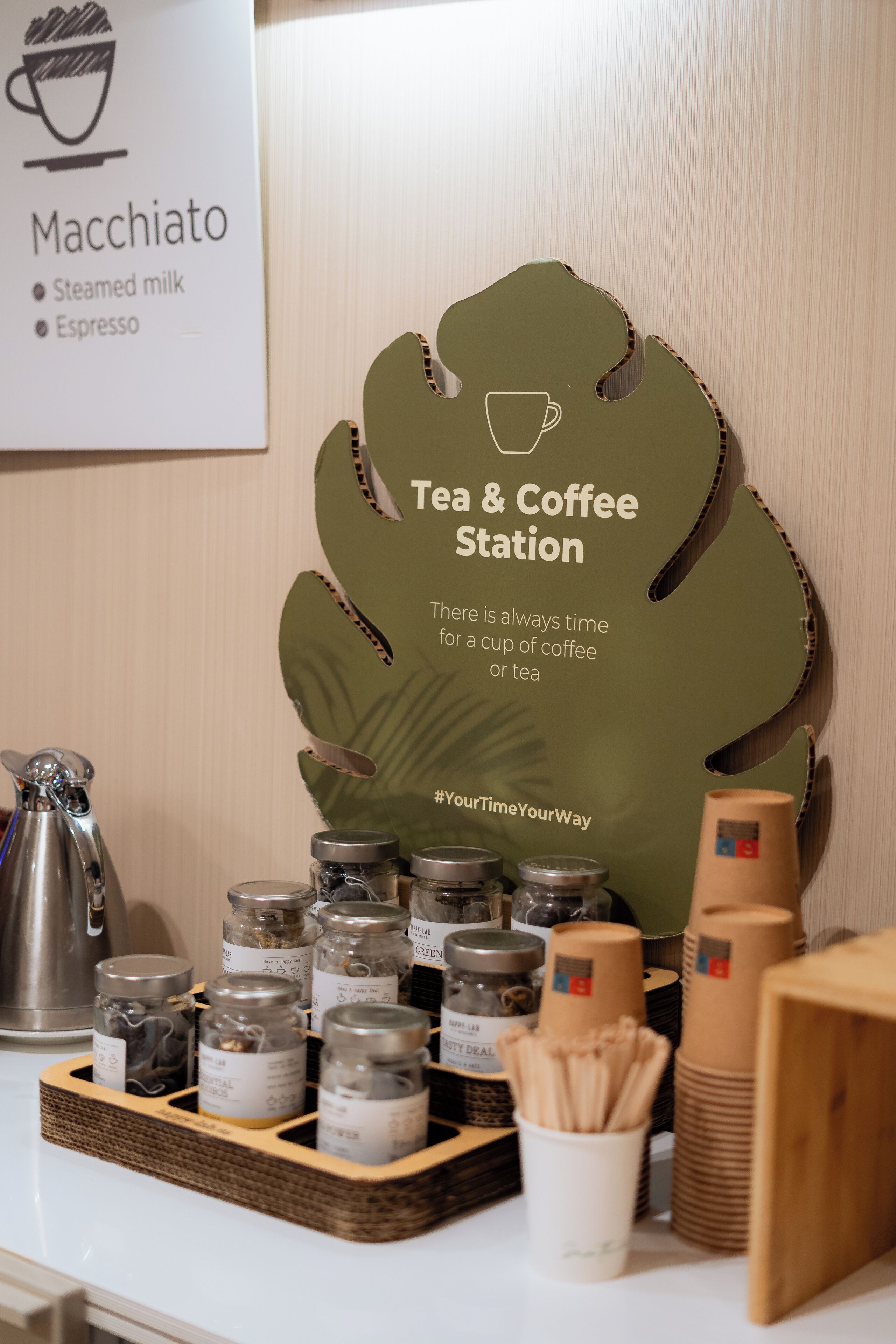 Cantinho de chá e café com sinalização, chá em potes e utensílios para preparar café.