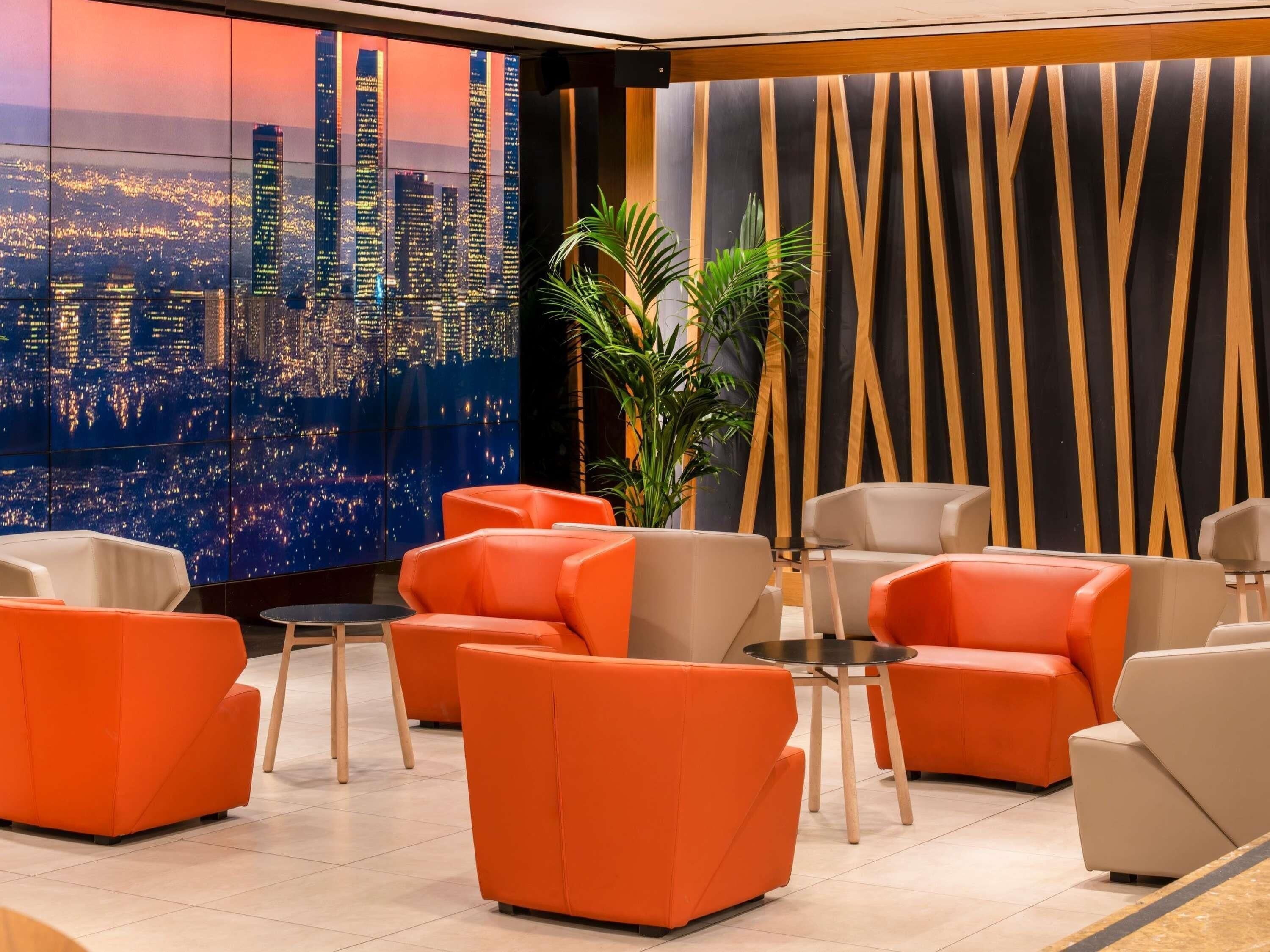 Un salon moderne avec des sièges orange, une vue sur la ville et un mur décoratif orné de lignes verticales.