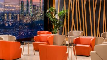 Un salon moderne avec des sièges orange, une vue sur la ville et un mur décoratif orné de lignes verticales.