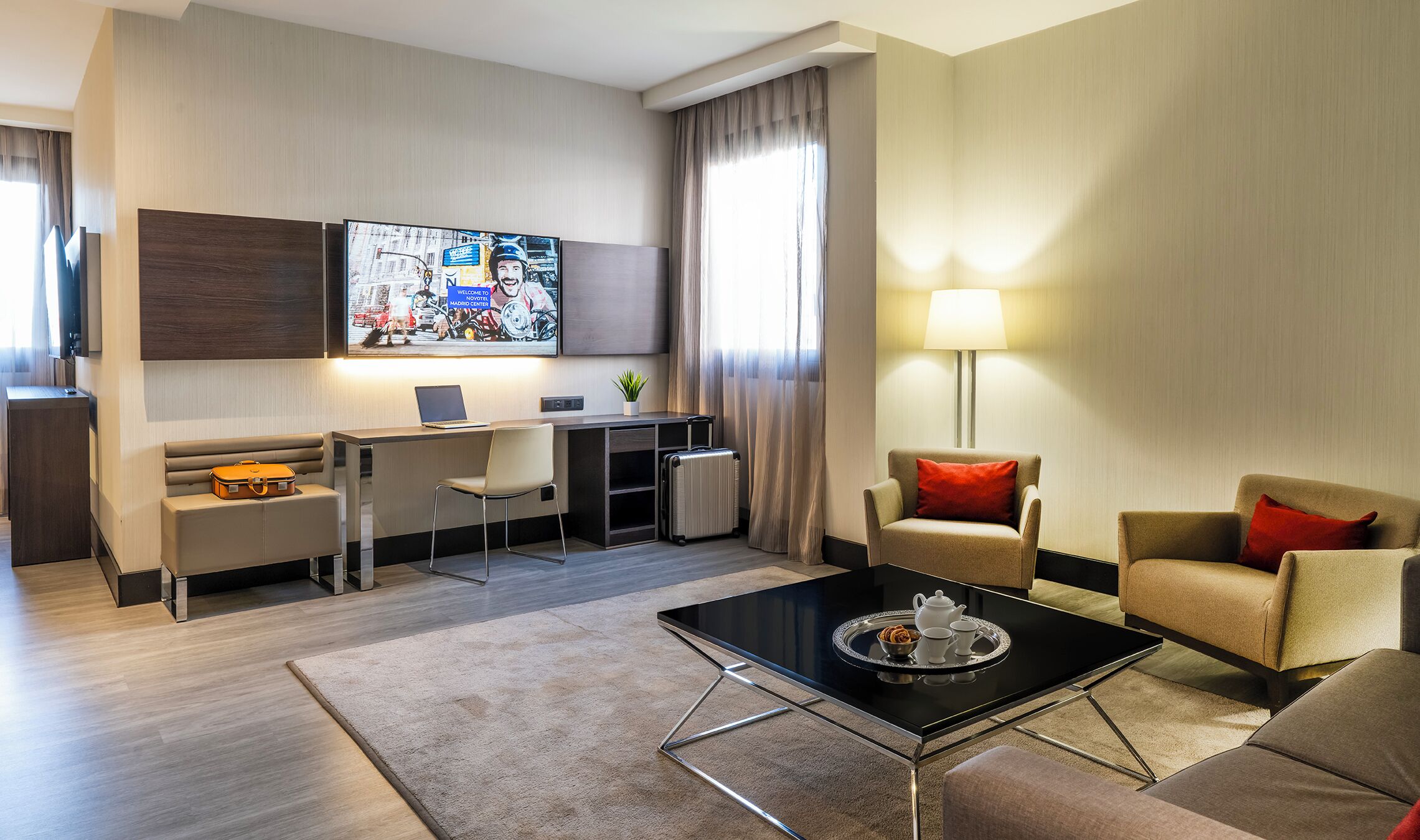 A modern hotel room with a desk, laptop, chair, sofa, and a coffee table with a tray.