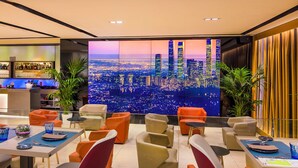 Un salon moderne offrant une vue sur la ville, avec des espaces de détente et un bar.