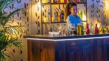 Un espace bar avec un barman, des étagères remplies de bouteilles d’alcool et différents types de verres.
