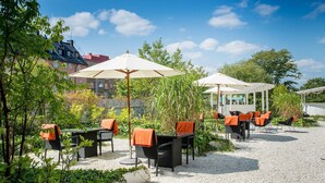 Un patio al aire libre con mesas y sillas, rodeado de vegetación y un edificio al fondo.