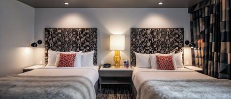 Habitación de hotel con dos camas, un cabecero estampado, una mesita de noche con lámpara y cortina estampada.