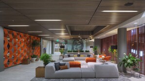 Un vestíbulo moderno con un sofá modular, plantas en macetas y un diseño geométrico en la pared.