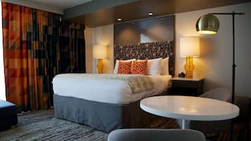 A hotel room with a bed, a round table, two lamps, and a patterned curtain.