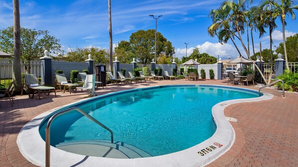 A swimming pool with lounge chairs and umbrellas, surrounded by palm trees and a fence. - Best Western Fort Myers Inn & Suites (Fort Myers)