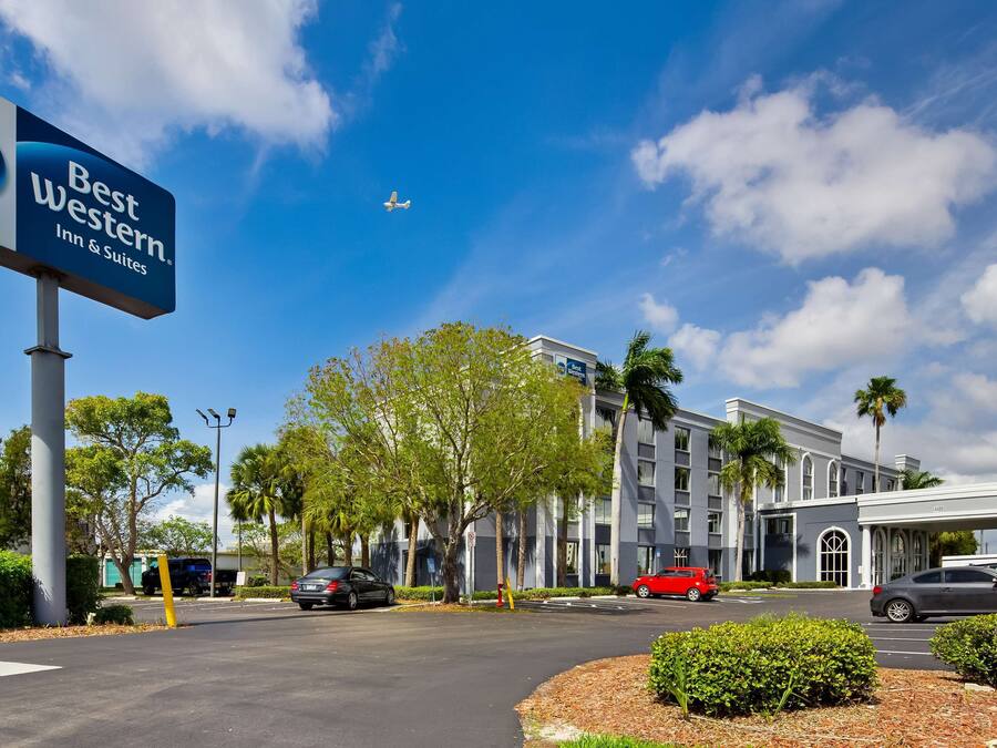 A Best Western Inn & Suites sign, a parking lot with cars, and a building with palm trees.