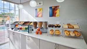 A breakfast buffet with various food options, including cereals, pastries, and a sign indicating gluten-free items.