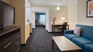 A hotel room with a TV, sofa, coffee table, desk, and a bathroom visible in the background.