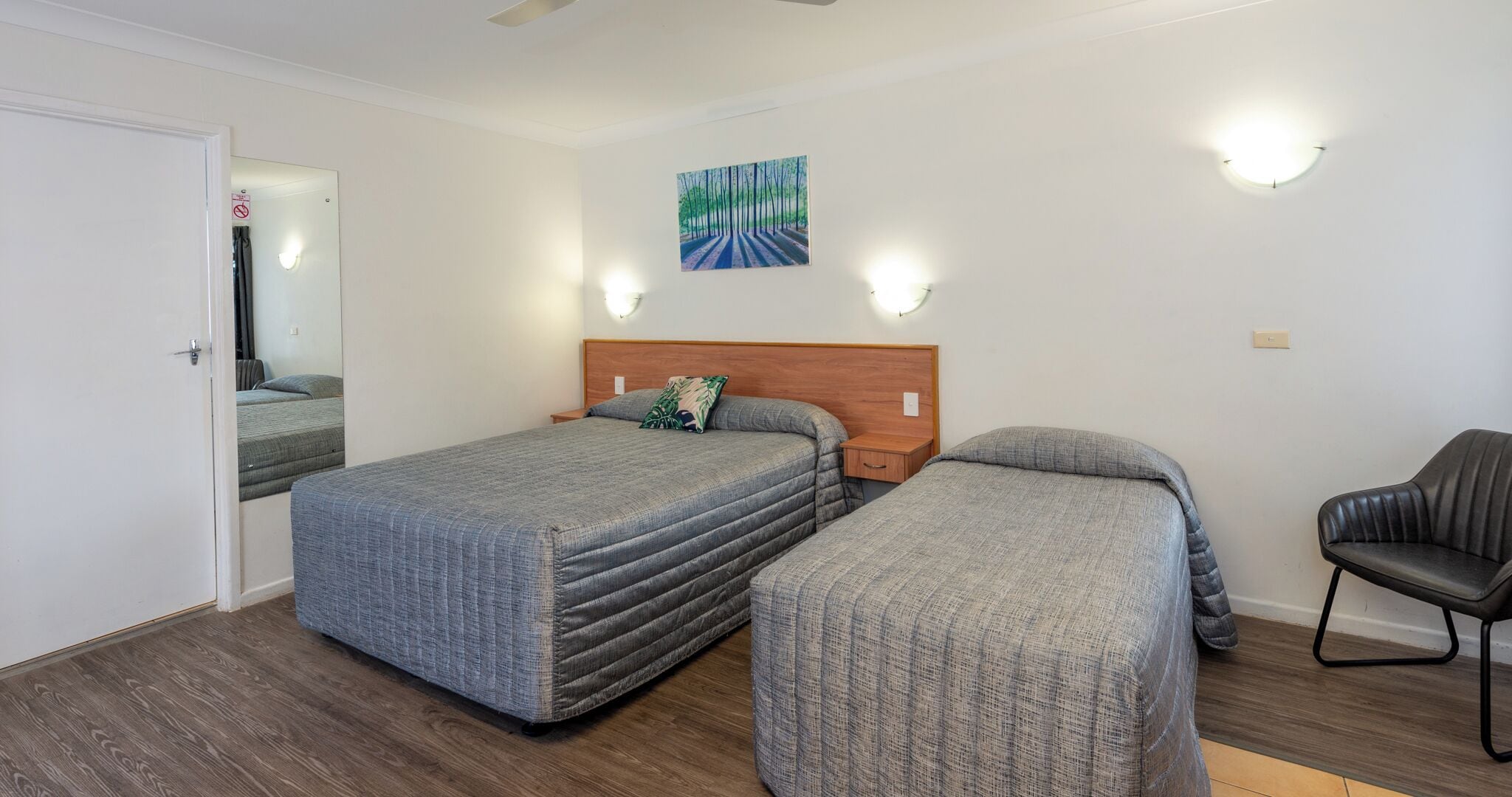 A room with two beds, a wooden headboard, a wall-mounted painting, and a chair.