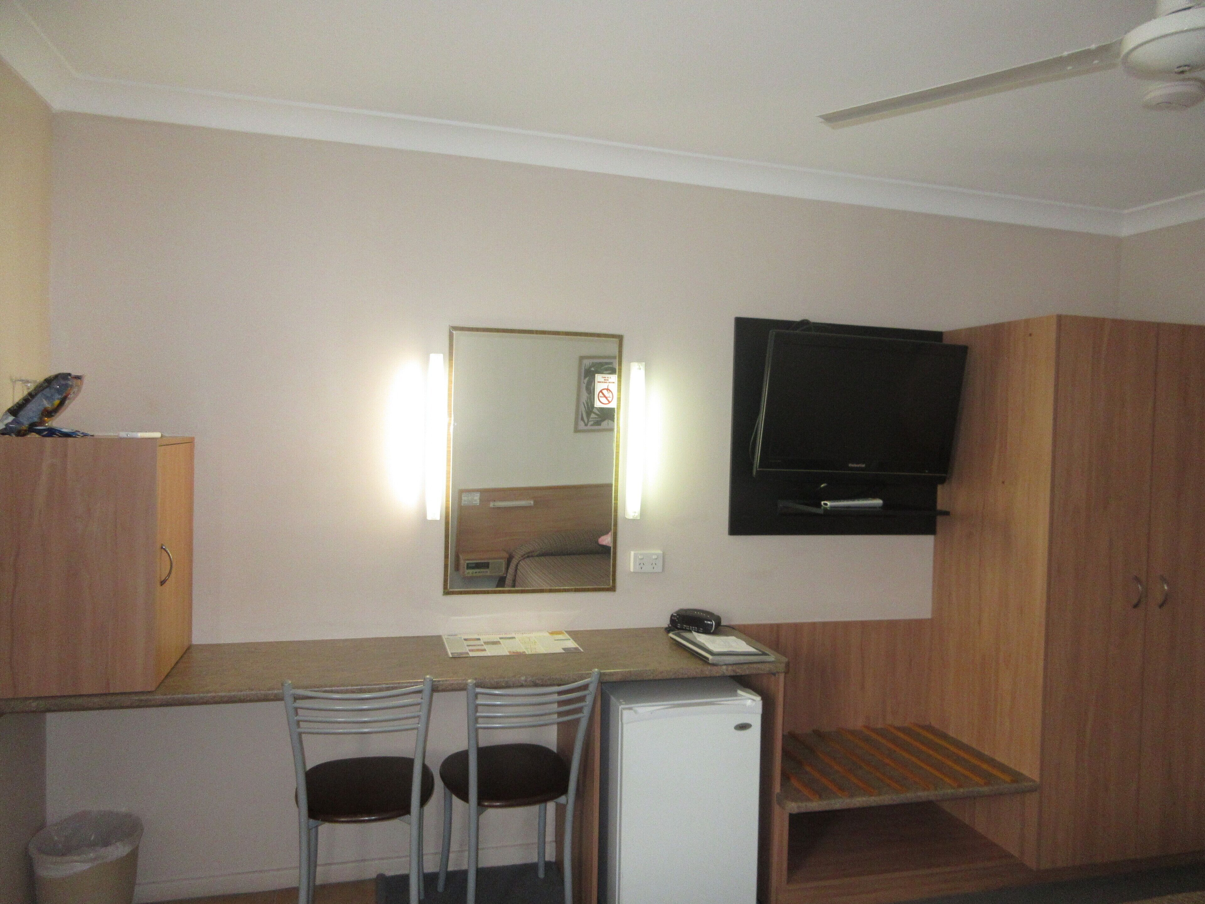 A compact kitchenette with a fridge, two chairs, a small table, and a mounted TV.