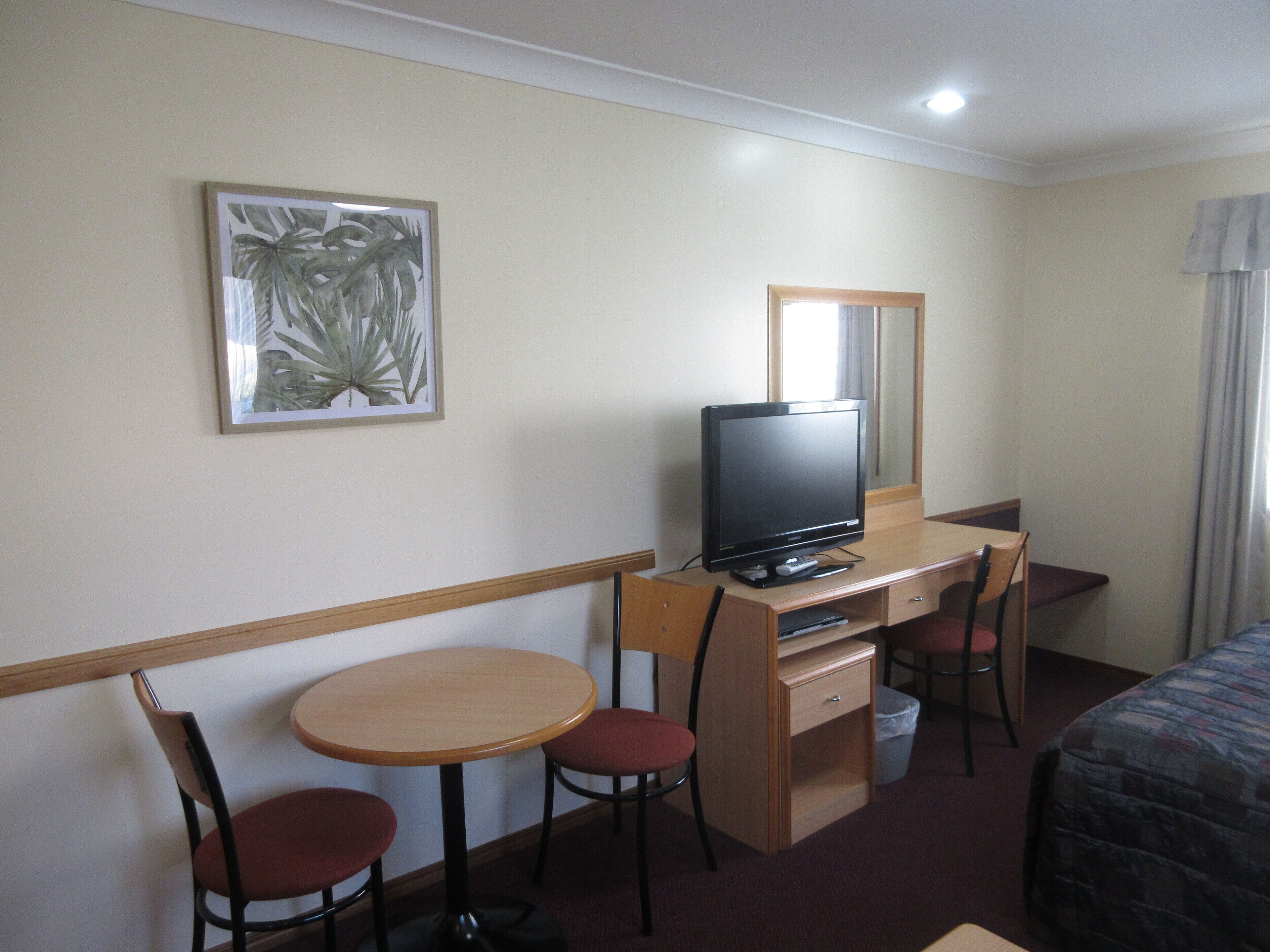 A hotel room with a wooden desk, a television, a chair, a small table, and a bed.