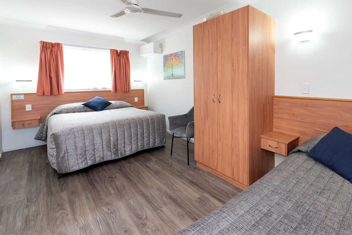 Two single beds with wooden headboards and nightstands, a grey chair, and a large wardrobe with a mirrored door.