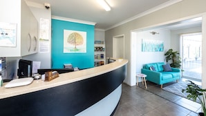A reception area with a curved counter, a teal wall, a tree painting, and a blue sofa in the background. - Riviera on Ruthven Motel (South Toowoomba)