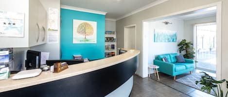 A reception area with a curved counter, a teal wall, a tree painting, and a blue sofa in the background.