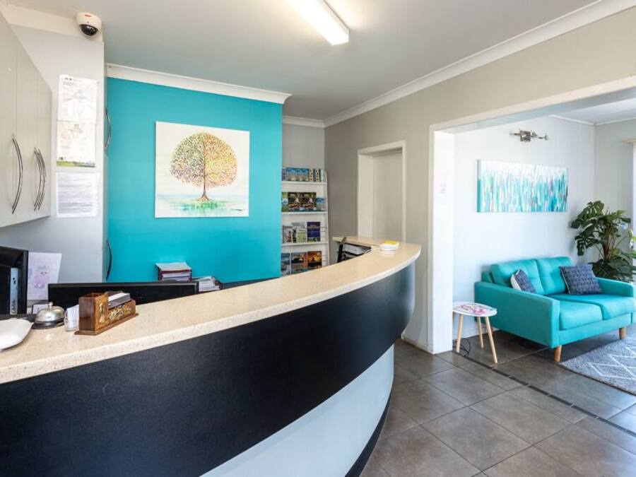 A reception area with a curved counter, a teal wall, a tree painting, and a blue sofa in the background.
