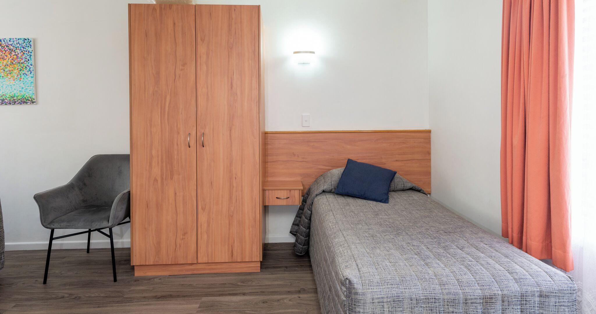 A bedroom with a bed, a chair, a wardrobe, and a nightstand.