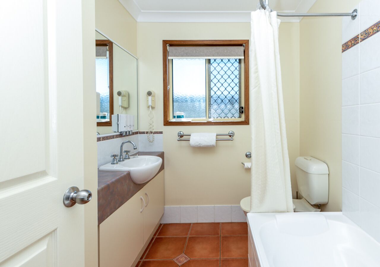Un baño con lavamanos, espejo, ventana y retrete.