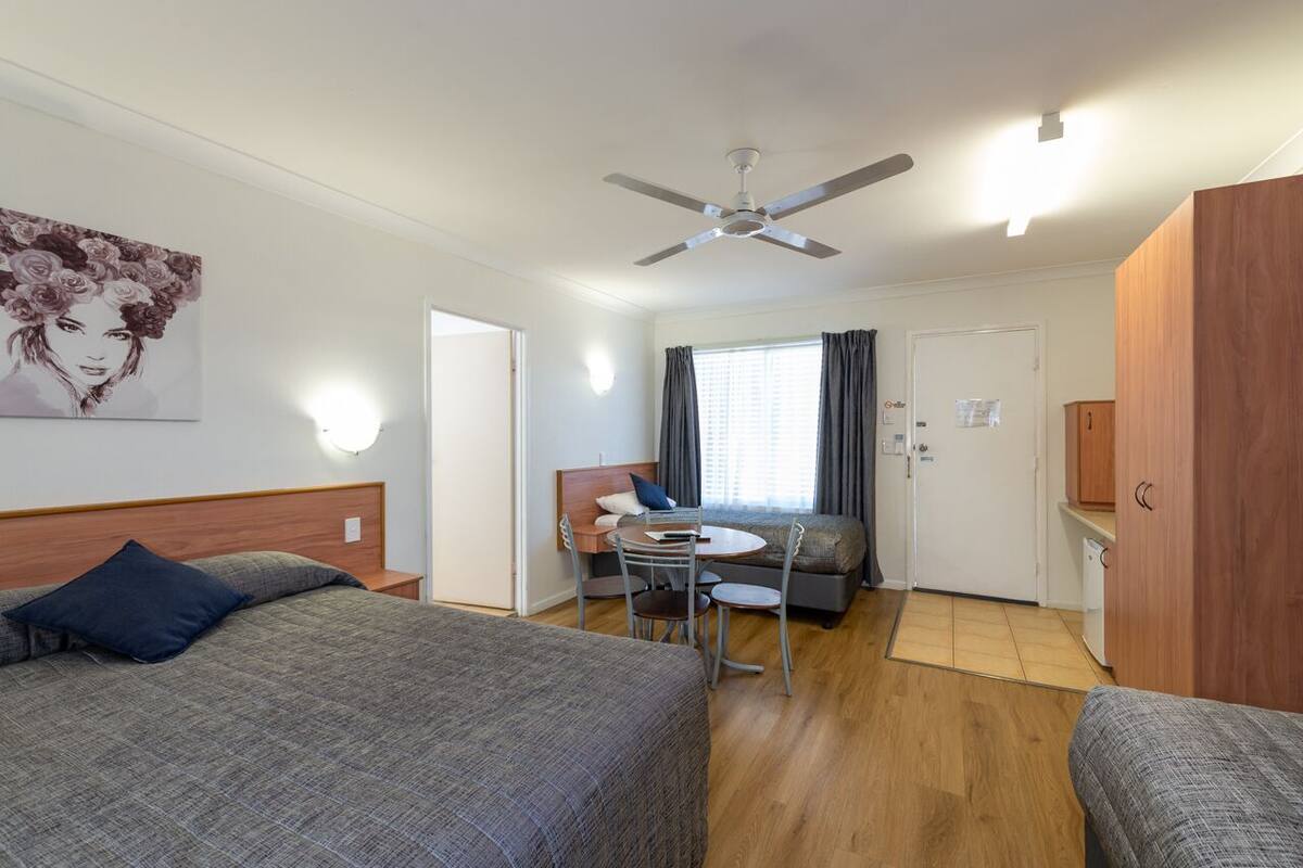 Una camera d'albergo con un letto, una scrivania, una sedia e una ventola a soffitto.