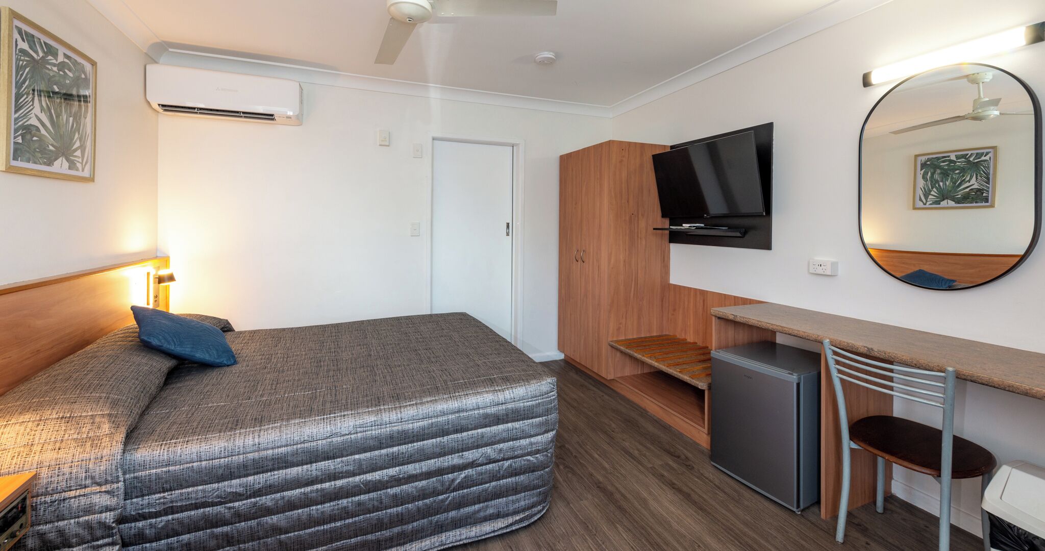 Una habitación de hotel pequeña con cama, escritorio, televisión y un refrigerador.