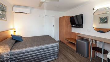 Una habitación de hotel pequeña con cama, escritorio, televisión y un refrigerador.