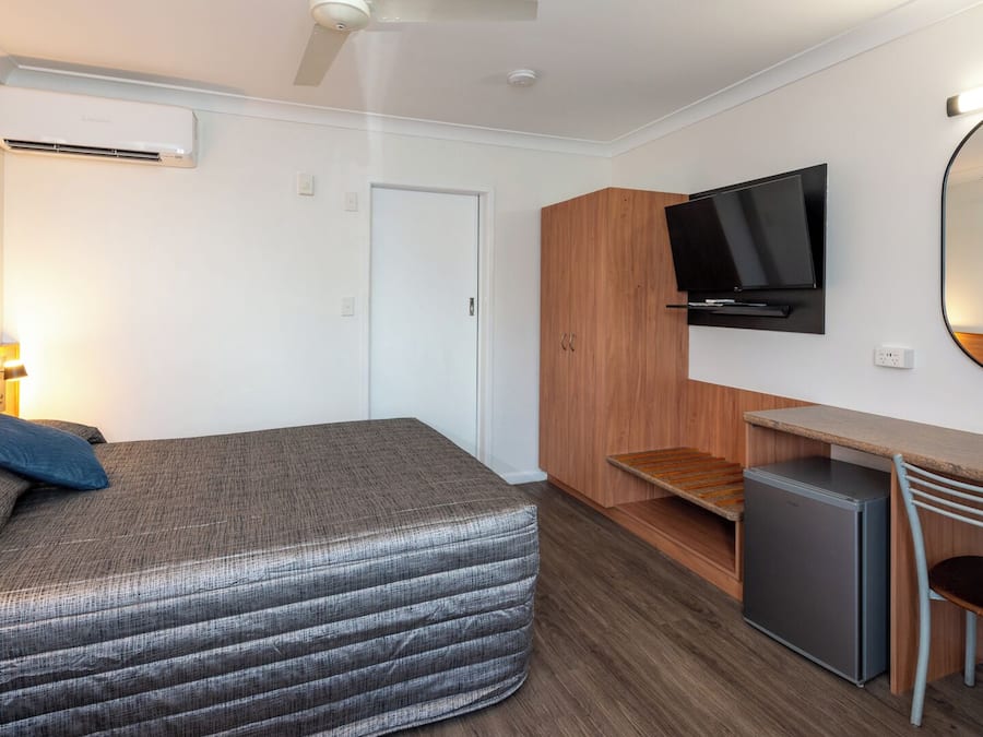 Une chambre d’hôtel de taille réduite, comprenant un lit, un bureau, une télévision et un petit réfrigérateur.