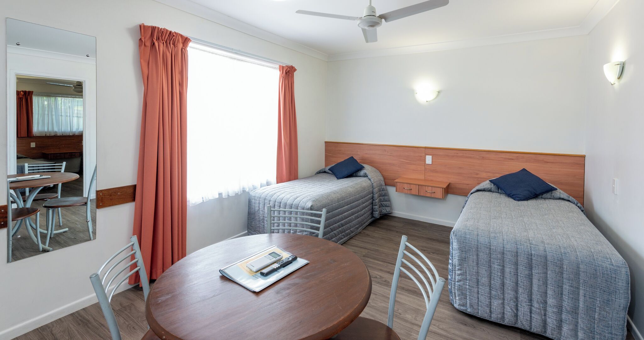 Een compacte hotelkamer met twee eenpersoonsbedden, een ronde eettafel en een plafondventilator.