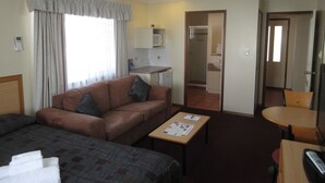 A hotel room with a sofa, a small table, a bed, a TV, and a kitchenette. - Riviera on Ruthven Motel (South Toowoomba)