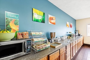 A commercial microwave oven, a food display with trays, and a coffee maker on a kitchen counter.