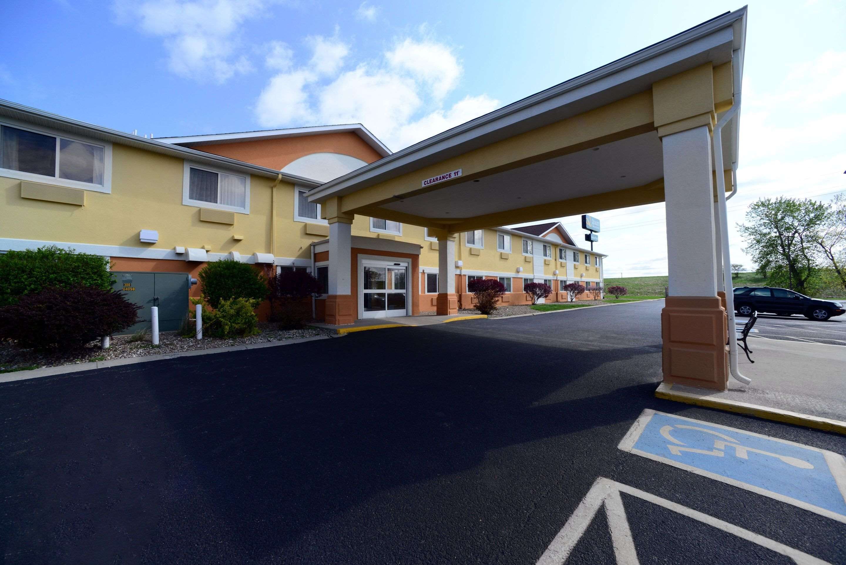 A hotel entrance with a covered parking area, marked handicap parking, and a clear sky.