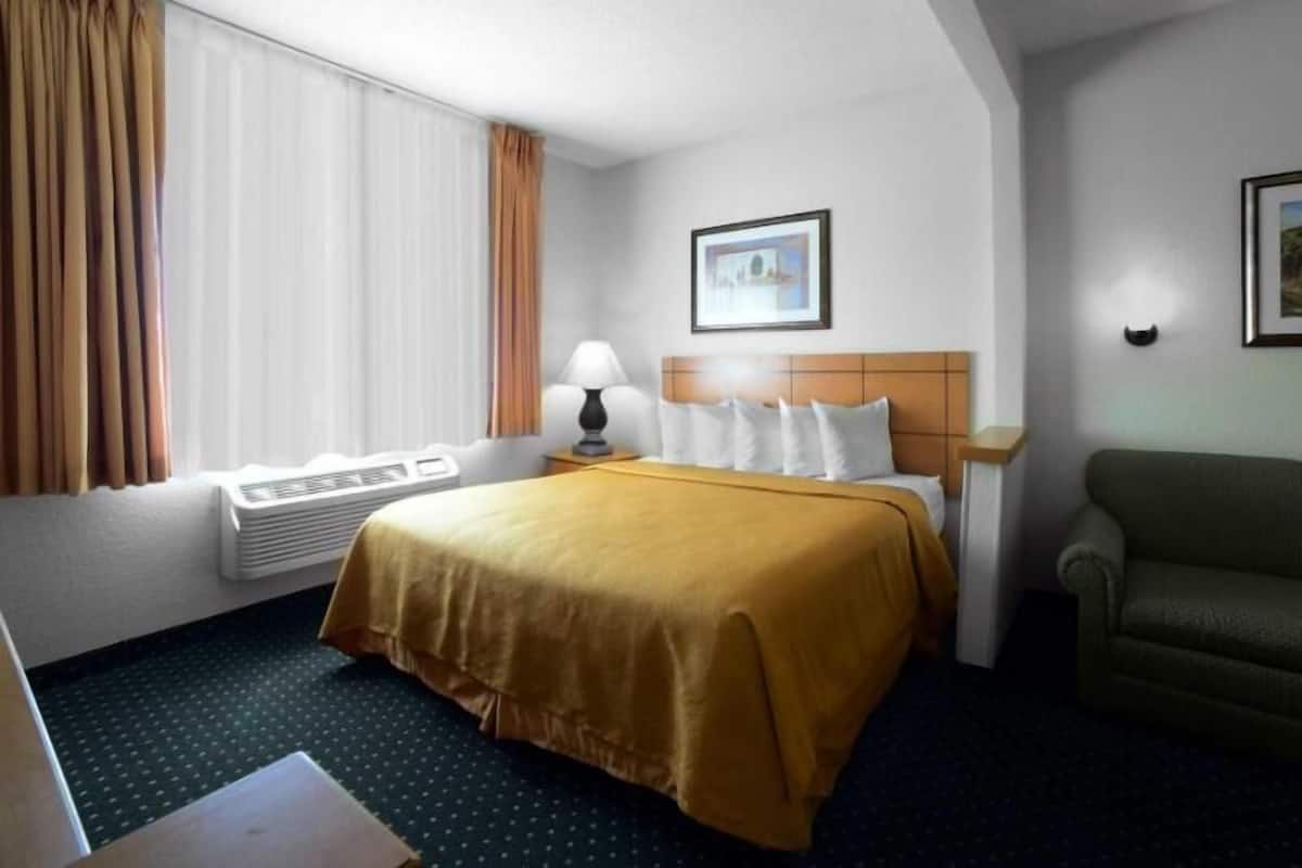 A hotel room with a bed, a desk, a chair, a lamp, and a picture on the wall.