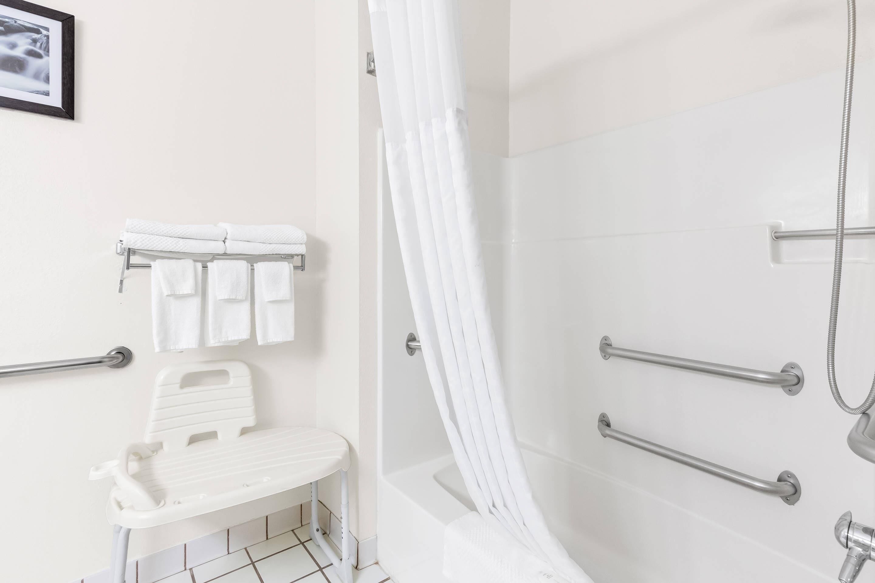 Ein Badezimmer mit Dusche, Haltegriffen, einer Sitzbank und einem Handtuchhalter.