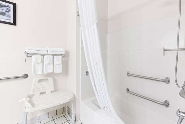 Ein Badezimmer mit Dusche, Haltegriffen, einer Sitzbank und einem Handtuchhalter.