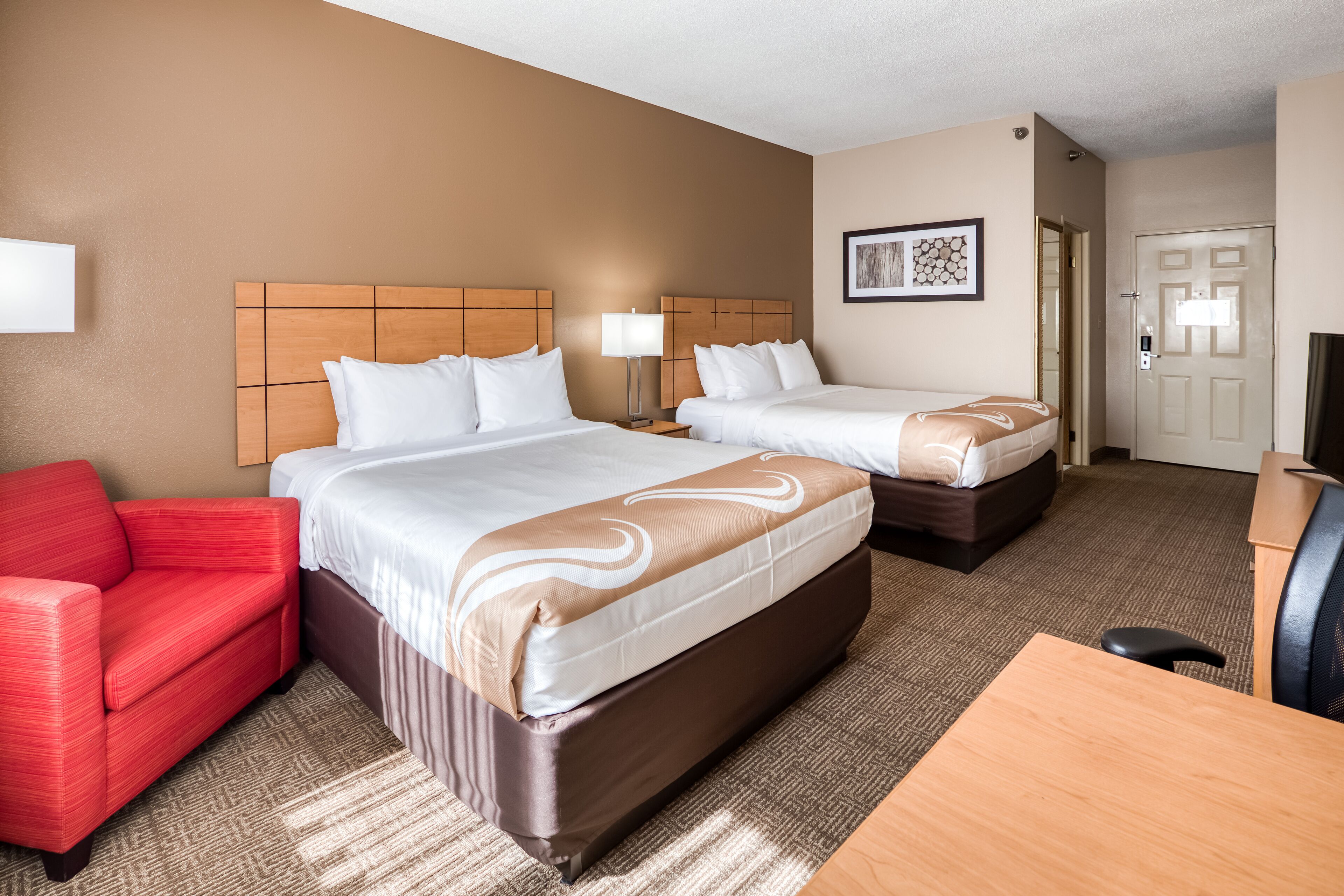 A hotel room with two beds, a red sofa, a desk, and a door.