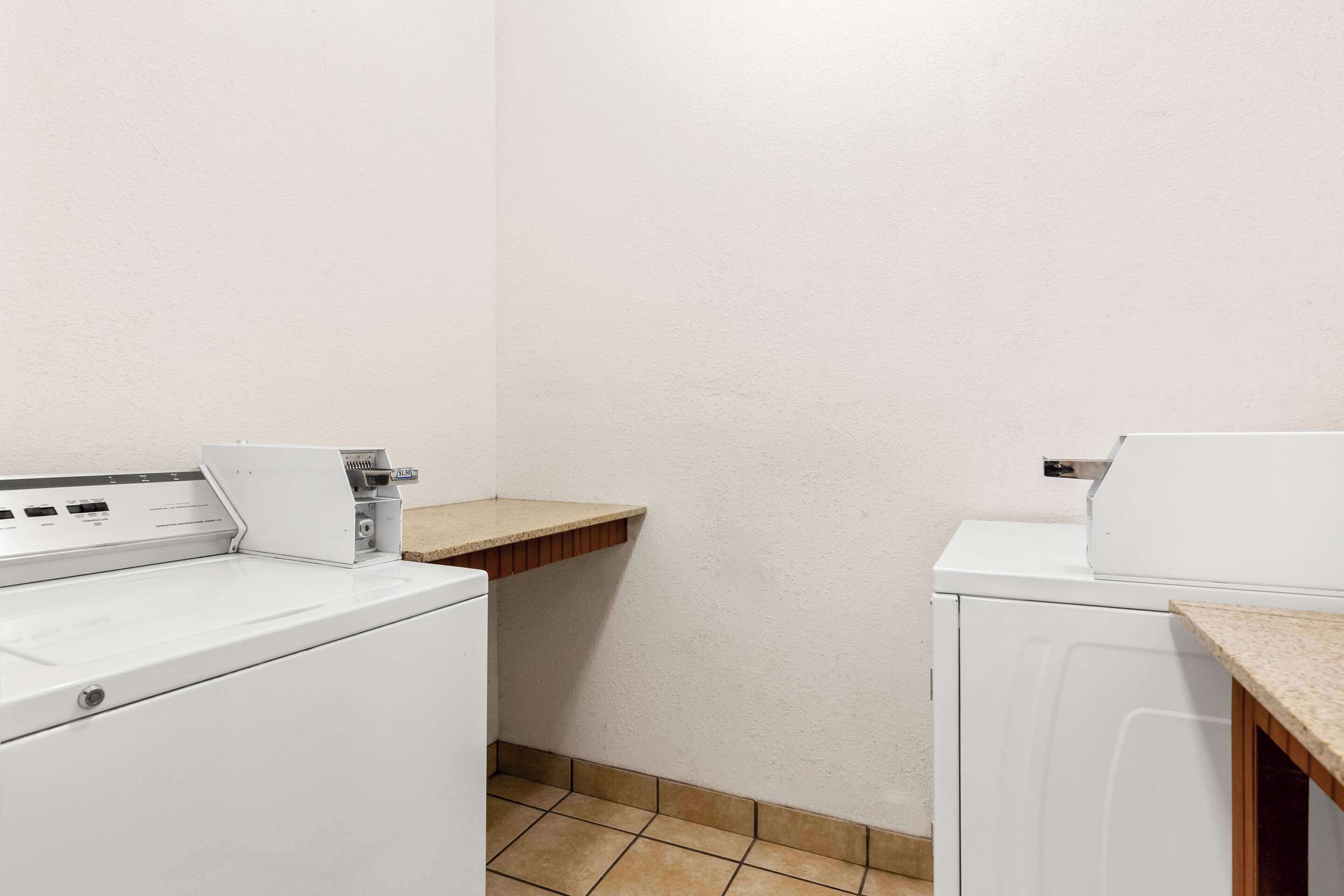 A laundry area with two white washing machines, a wooden shelf, and a tiled floor.