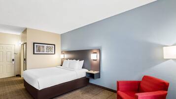 A hotel room with a bed, a nightstand, a red chair, and a wall-mounted light fixture.