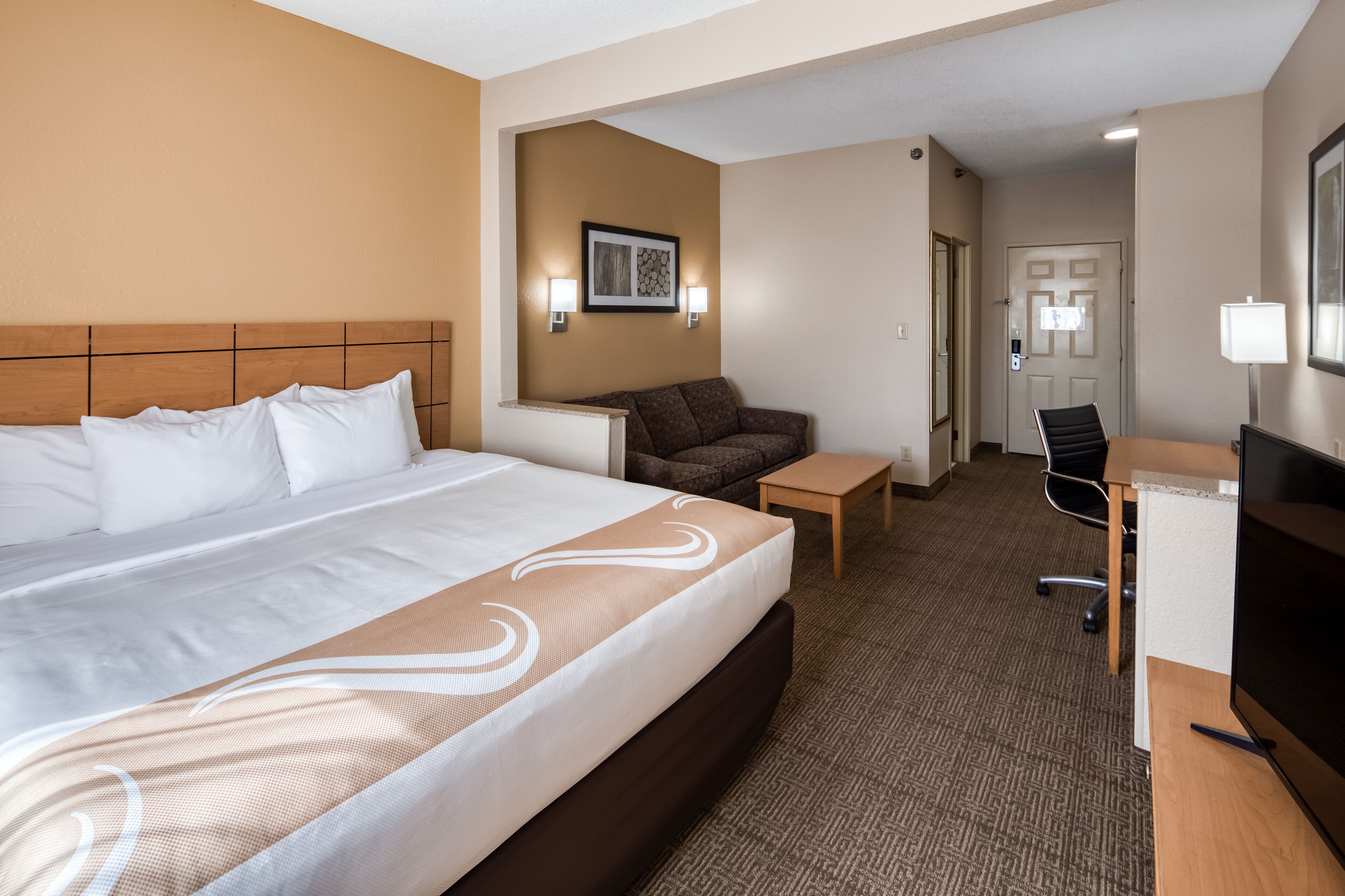 A hotel room with a large bed, a desk, a chair, a small table, and a couch.
