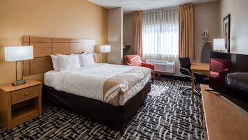 Una habitación de hotel con una cama grande, un escritorio, una silla, un televisor y una lámpara de escritorio.