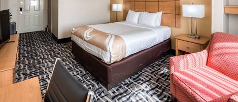 Habitación de hotel con una cama grande, mesitas de noche con lámparas, un escritorio, una silla y un sillón rojo.