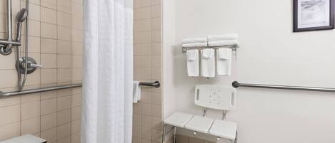 A bathroom with a shower, grab bars, a toilet, and a sink.