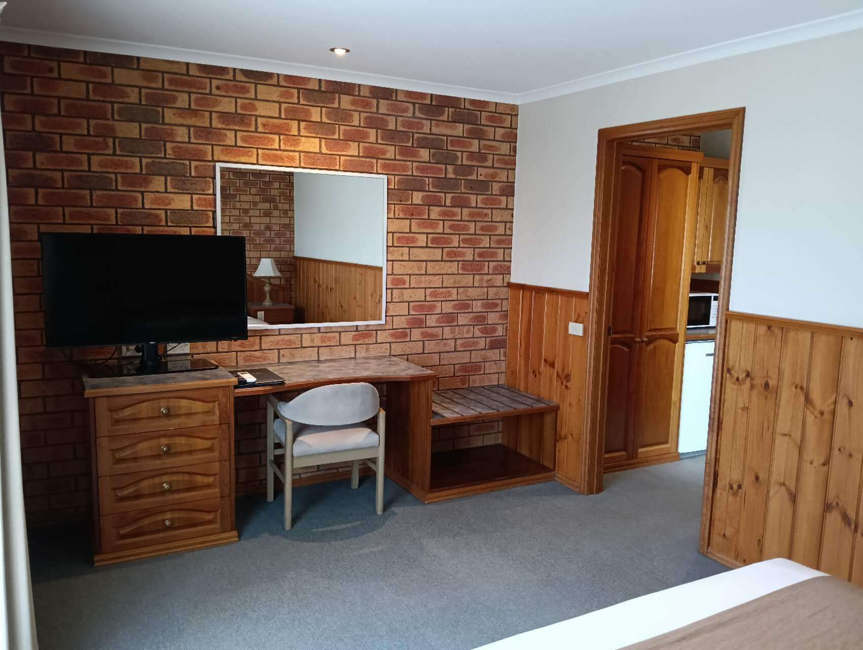 Una habitación con pared de ladrillo, un escritorio de madera con silla, televisión y armario.