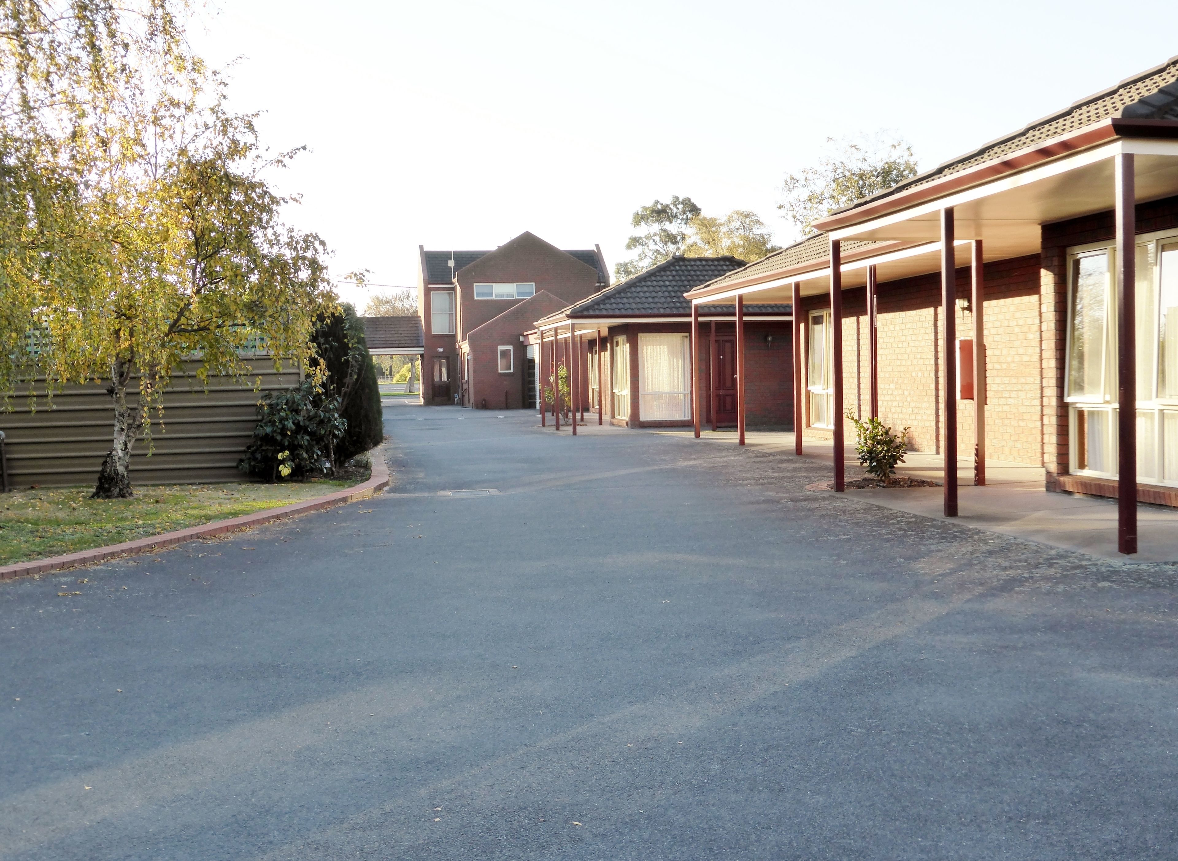 A row of motel-style buildings with a covered walkway and a paved driveway.