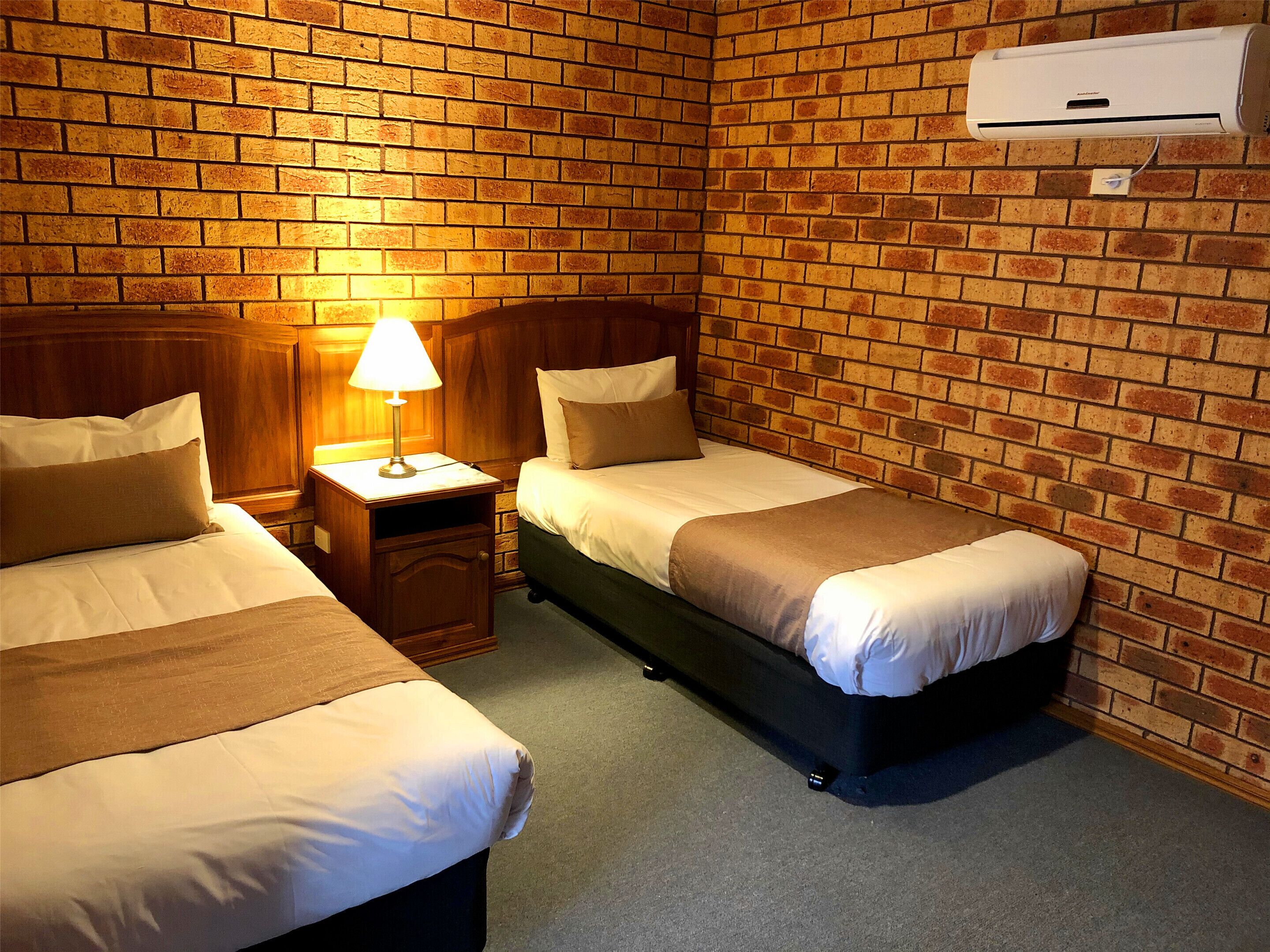 Een kamer met twee bedden, een nachtkastje met een lamp en een bakstenen muur.