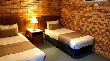 Een kamer met twee bedden, een nachtkastje met een lamp en een bakstenen muur.