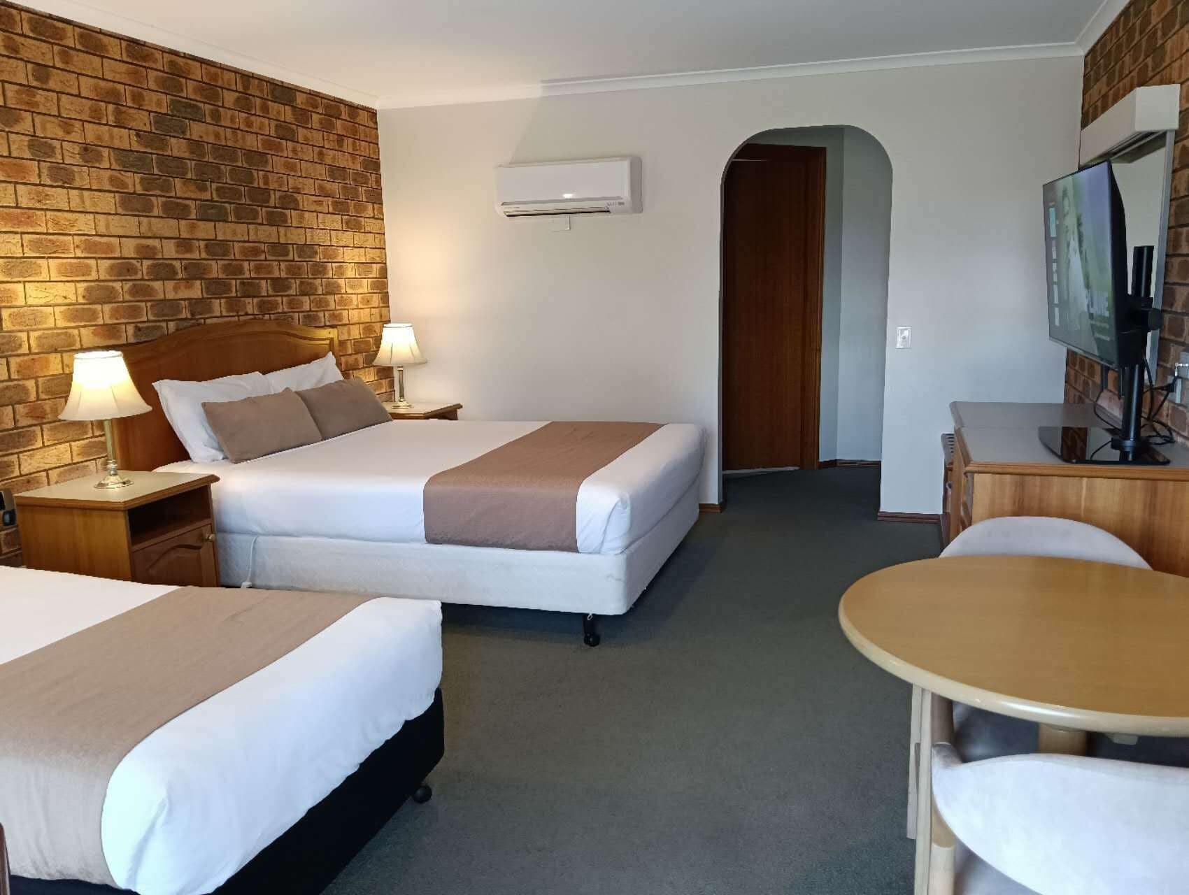 A hotel room with two beds, a TV, a desk, and an air conditioning unit.